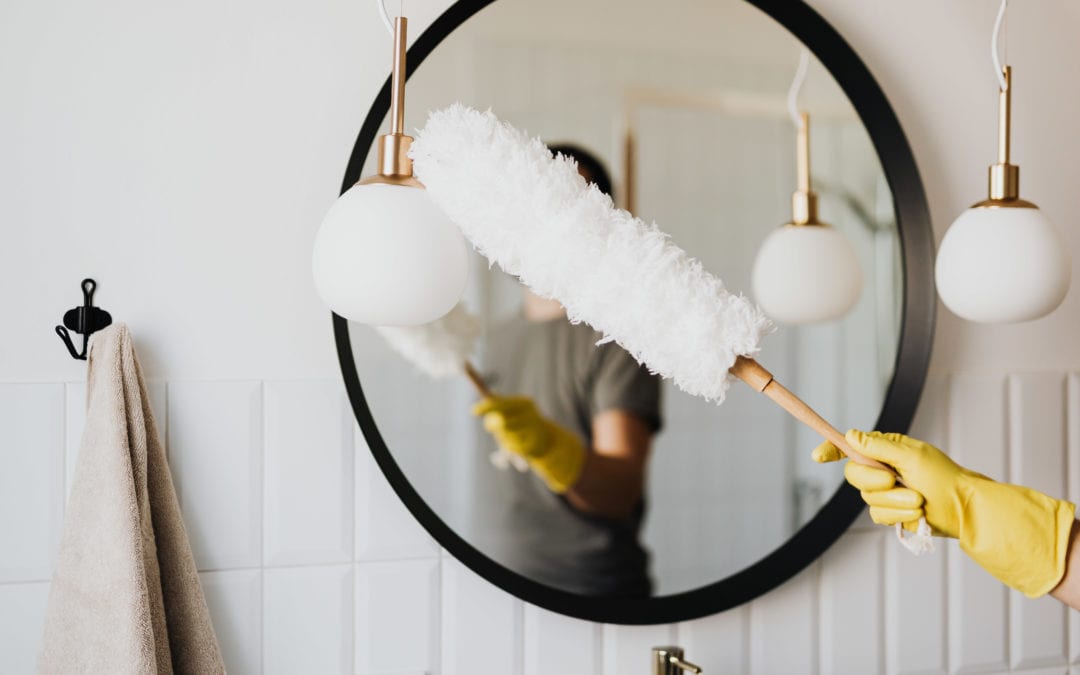 cleaner dusting of oval shaped mirror in bathroom, guide to keeping your house clean and organised
